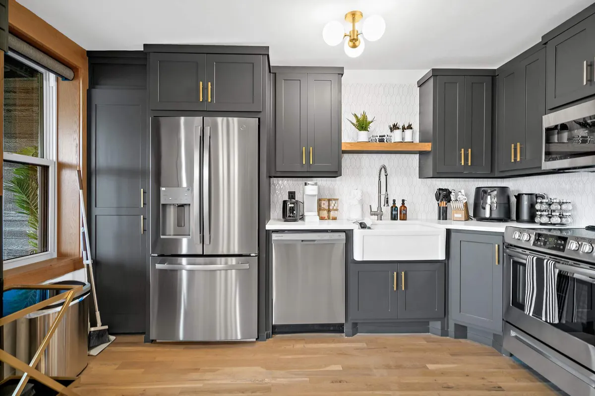 A spacious, modern kitchen with a stainless steel refrigerator, farmhouse sink, kitchen island, and open shelving. The area is designed for cooking, entertaining, and spending quality time with family or friends.