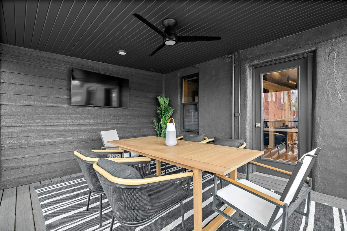 A stylish, open dining space featuring a modern table, sleek black ceiling fan, television, and potted plant. The area conveys a sense of sophistication and is designed for both dining and casual entertaining.