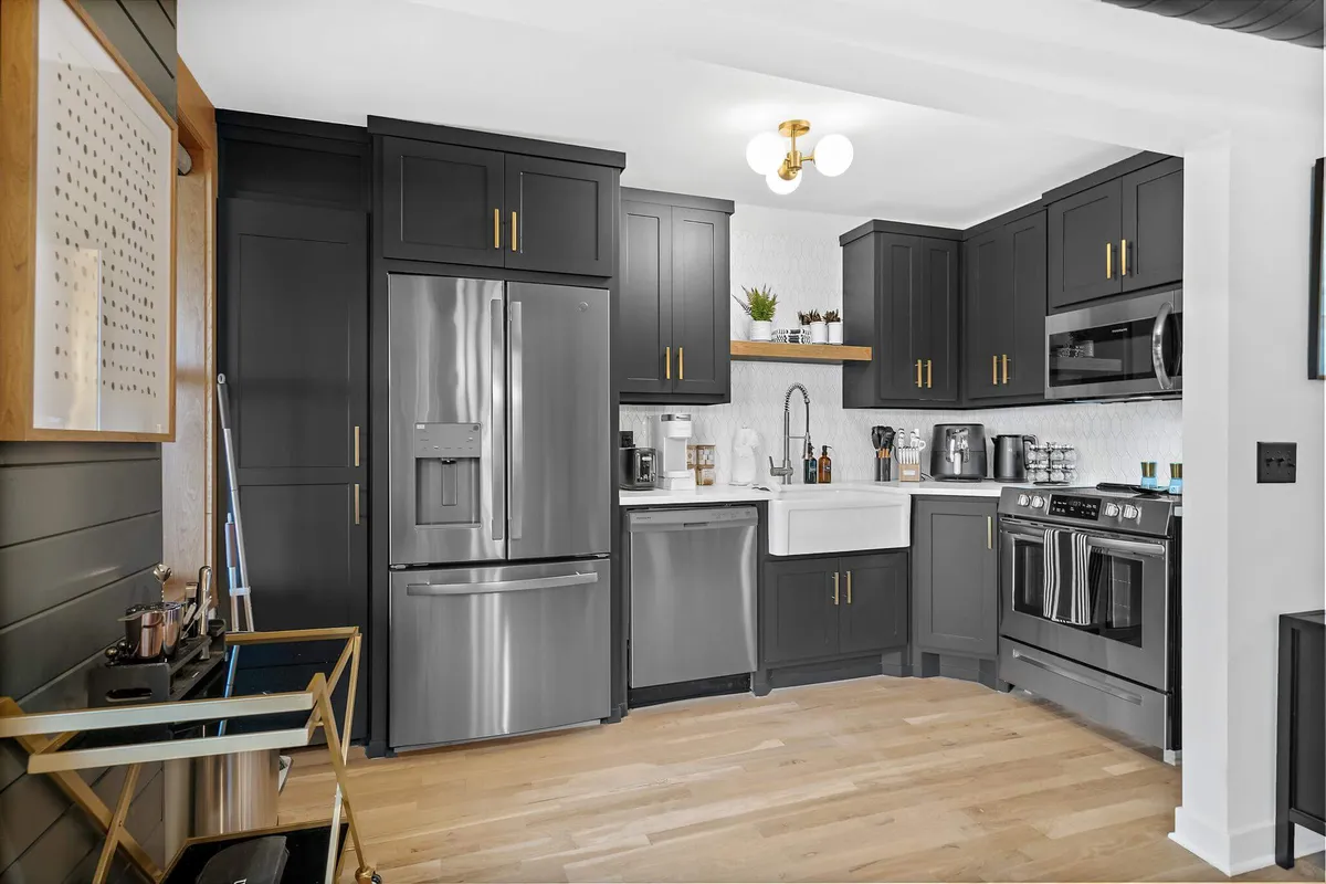 A sophisticated kitchen with black cabinetry, stainless steel appliances, open shelving, a farmhouse sink, and gold hardware details. The layout is both stylish and functional, perfect for culinary adventures and entertaining.
