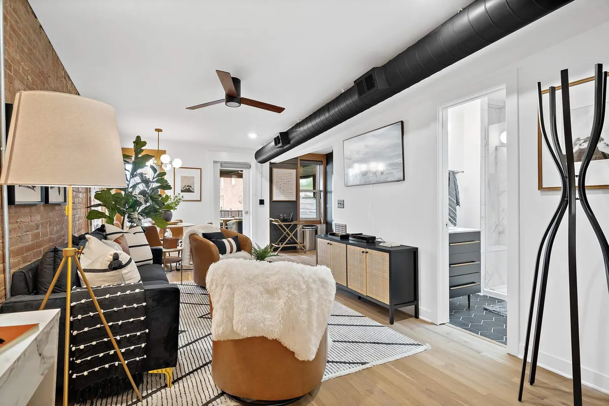 A cozy, modern living area featuring a sofa and armchair arranged for conversation or relaxation, complemented by a green plant and stylish lighting. The dining area is visible in the background, creating a sense of openness and connection.