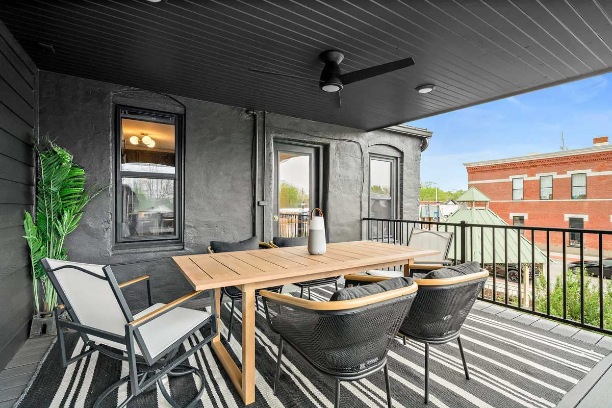 A welcoming outdoor dining area with a table and chairs arranged on a patio, surrounded by lush greenery. The setting basks in natural light, suggesting a tranquil spot for enjoying meals or drinks while soaking in the ambiance of the neighborhood.