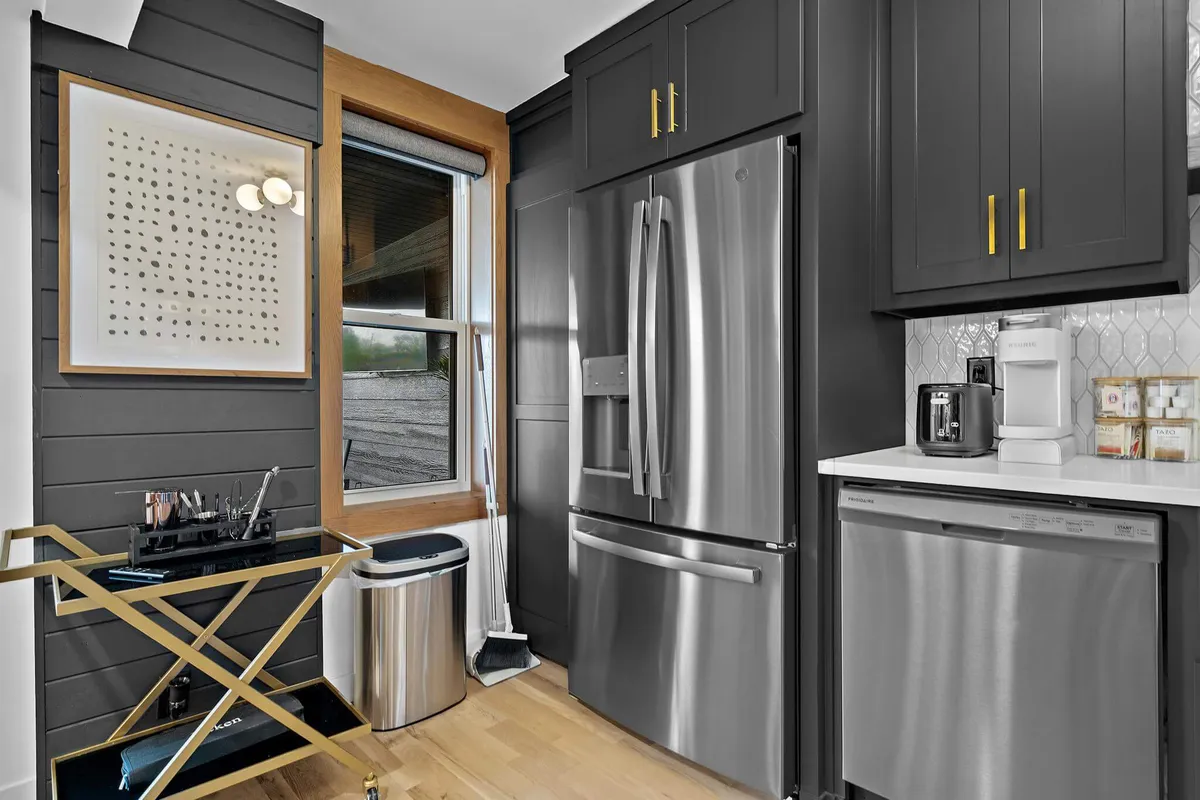 This image showcases a kitchen area with a stainless steel refrigerator, a gold-accented cart, modern artwork on the wall, and a bright window letting in natural daylight. The scene suggests a lively, welcoming space ideal for preparing meals before or after a city outing, with visible touches of contemporary style and urban flair.